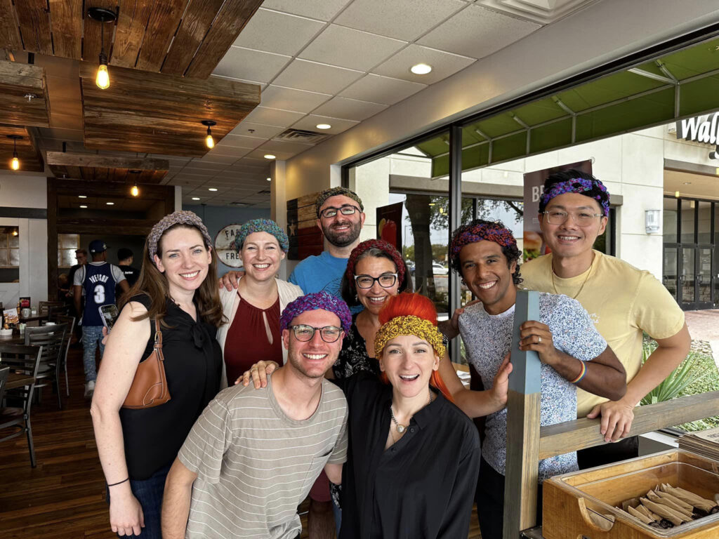 Composers Dale Trumbore, Jocelyn Hagen, Michael Schachter, Abbie Betinis, Carlos Cordero, Saunder Choi, Alex Berko, and Shara Nova pose for a photo wearing their crocheted crowns.